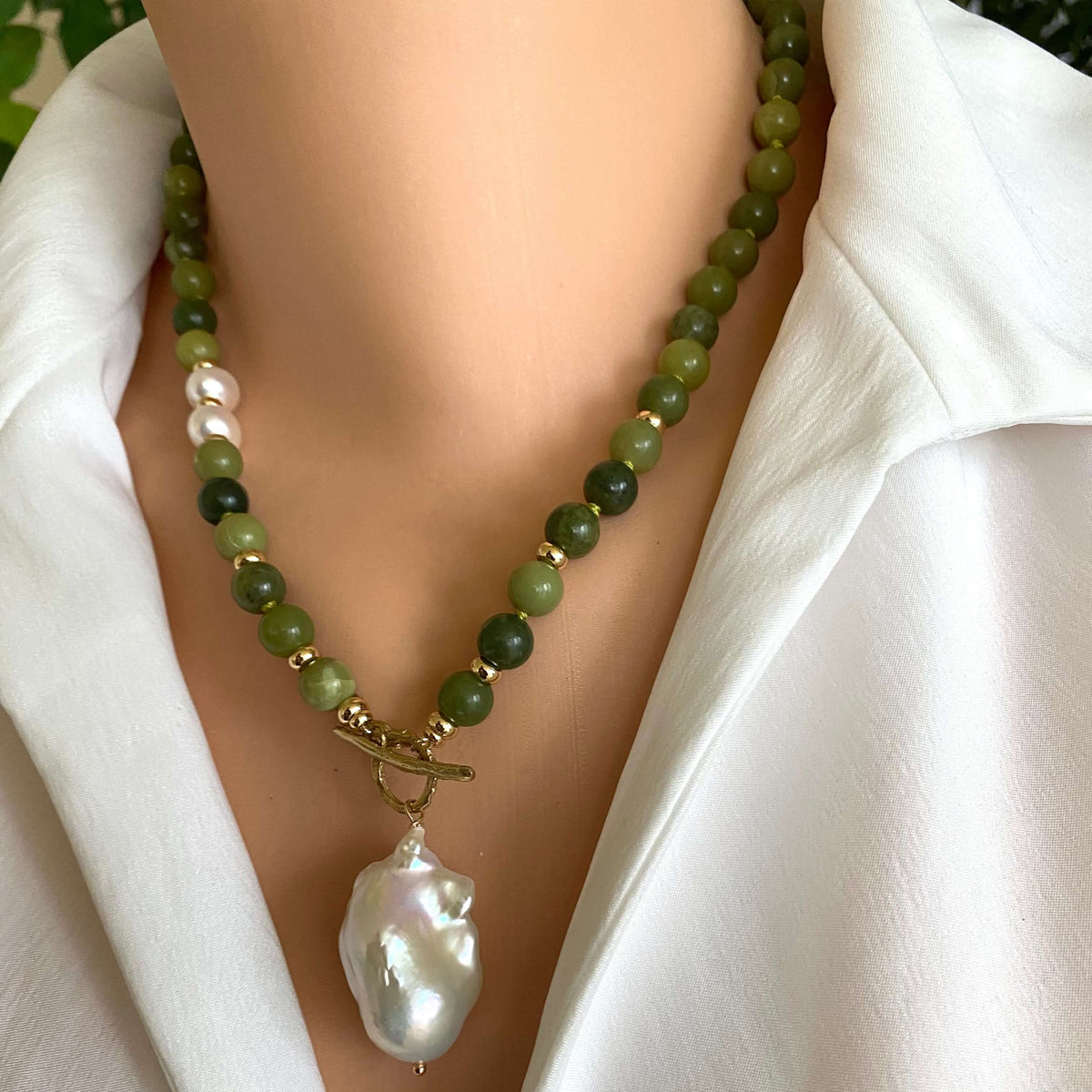 Necklace with green beads and a large white pearl pendant on a mannequin wearing a white shirt.