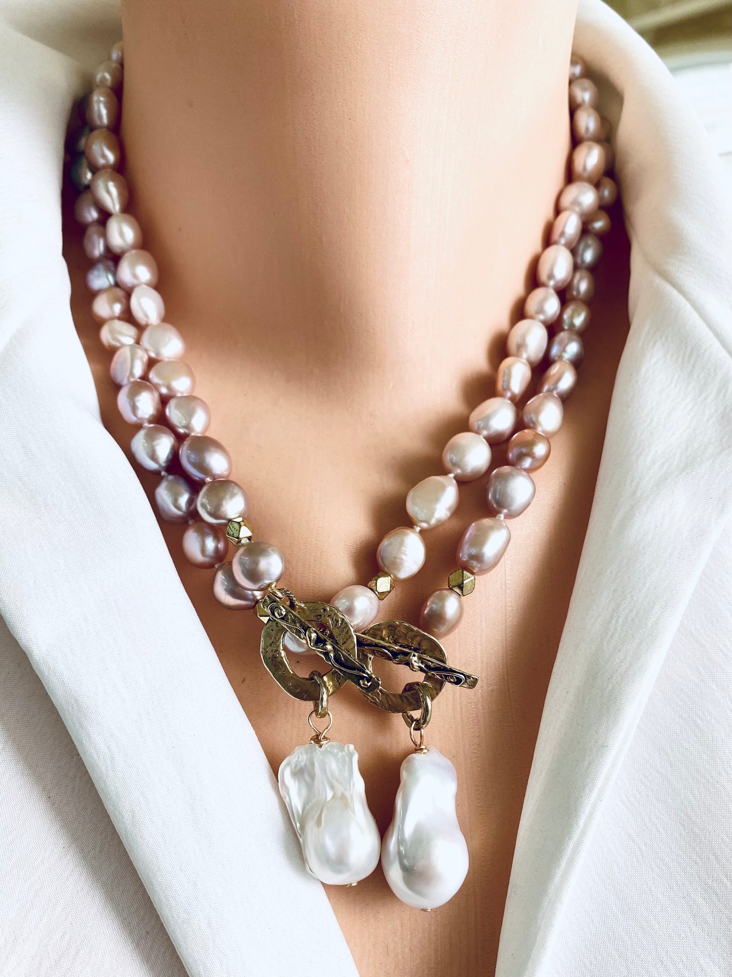 Two pink pearl necklaces with baroque pendants worn on mannequin, frontal view
