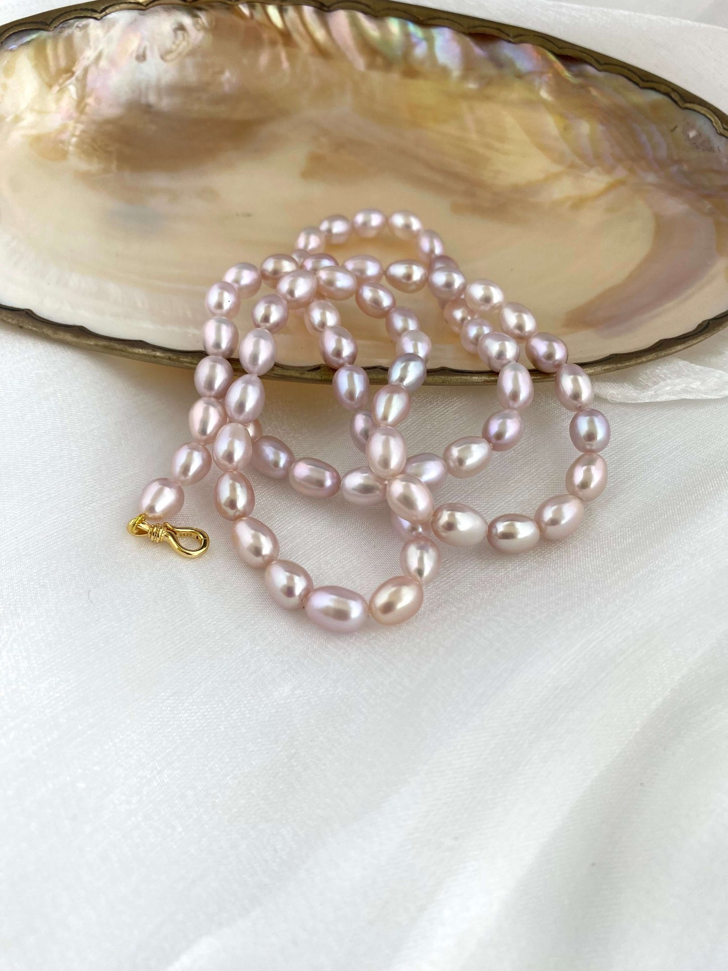 Pearl necklace on a white surface with an open shell in the background