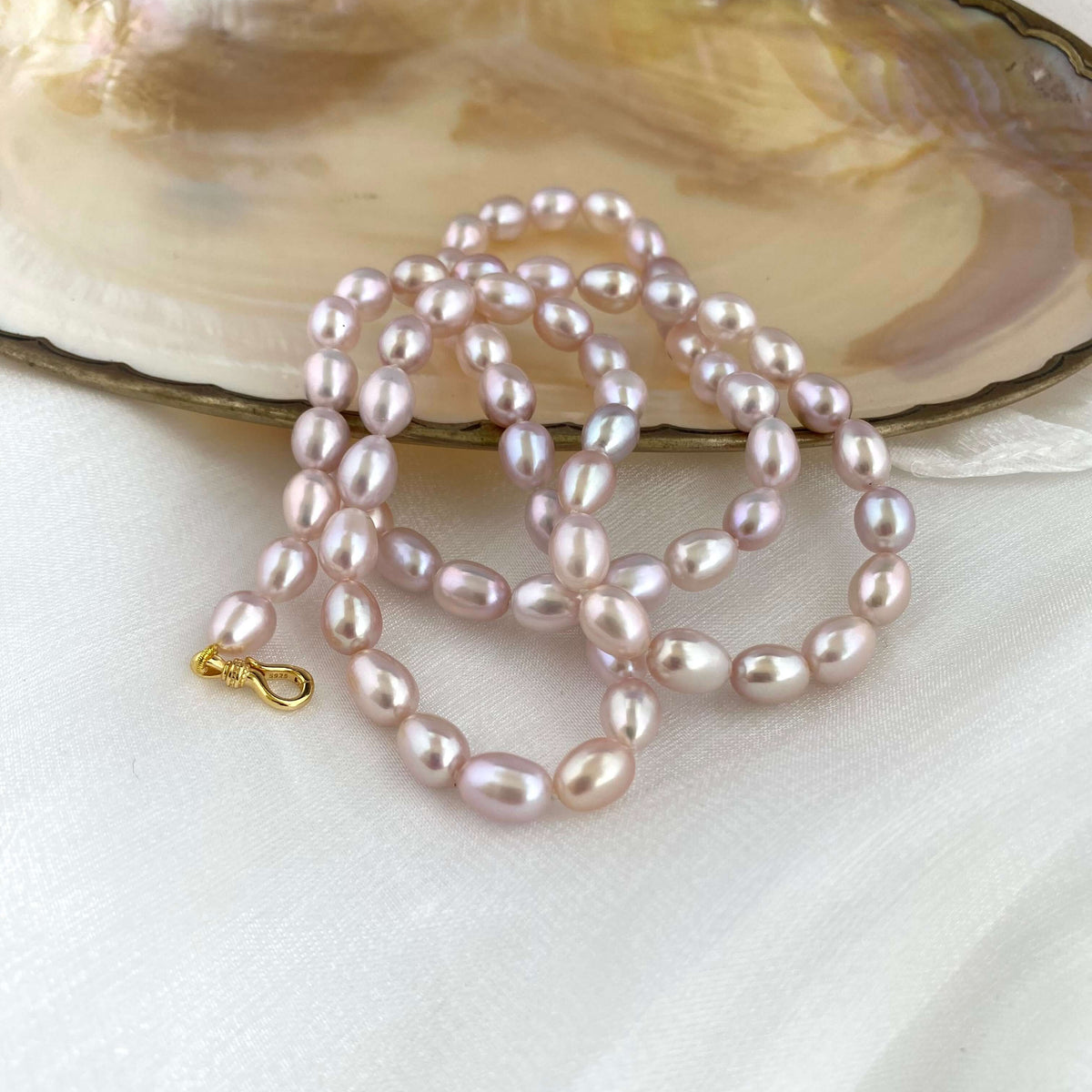 Pearl necklace on a white surface with an open shell in the background
