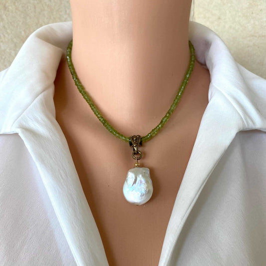 A close-up of a person wearing a green beaded necklace with a large, irregular white baroque pearl pendant, styled with a white collared shirt.