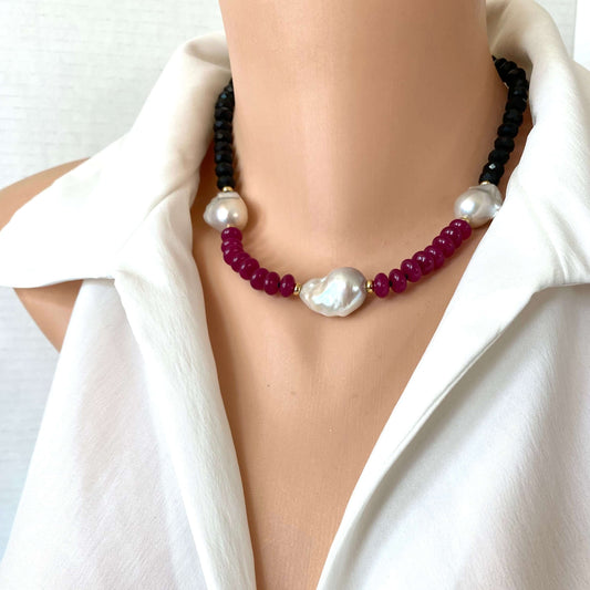 A close-up of a beaded necklace displayed on a mannequin torso wearing a white blouse, dark black beads with deep red beads, accented by white pearls.