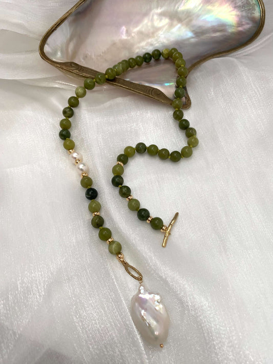 Necklace with green beads and a large pearl pendant on a white fabric background