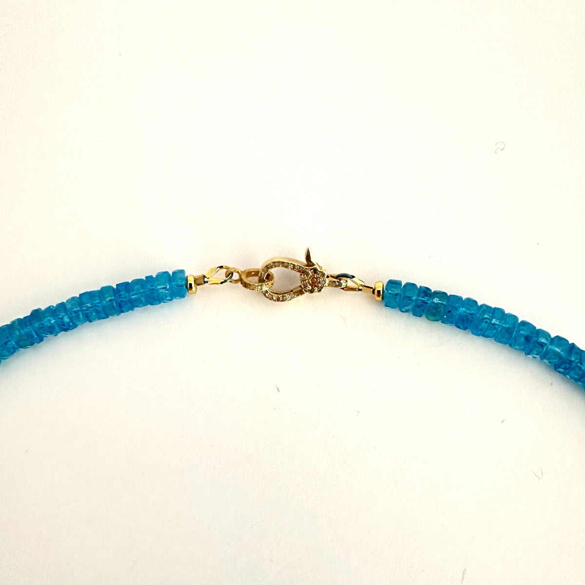 A close-up of a beaded necklace featuring bright blue faceted beads and a gold-toned lobster clasp with a clear stone, set against a plain white background.