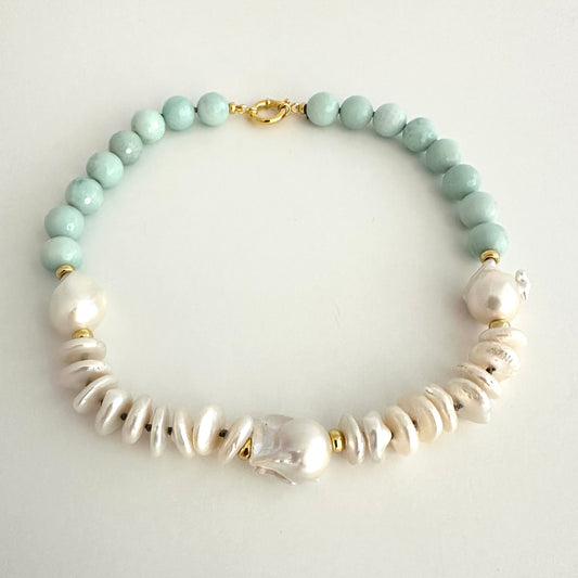 A beaded necklace featuring light mint green round beads, white baroque pearls, and textured white disc beads, accented with small gold spacer rings and a gold clasp, displayed on a light gray background.