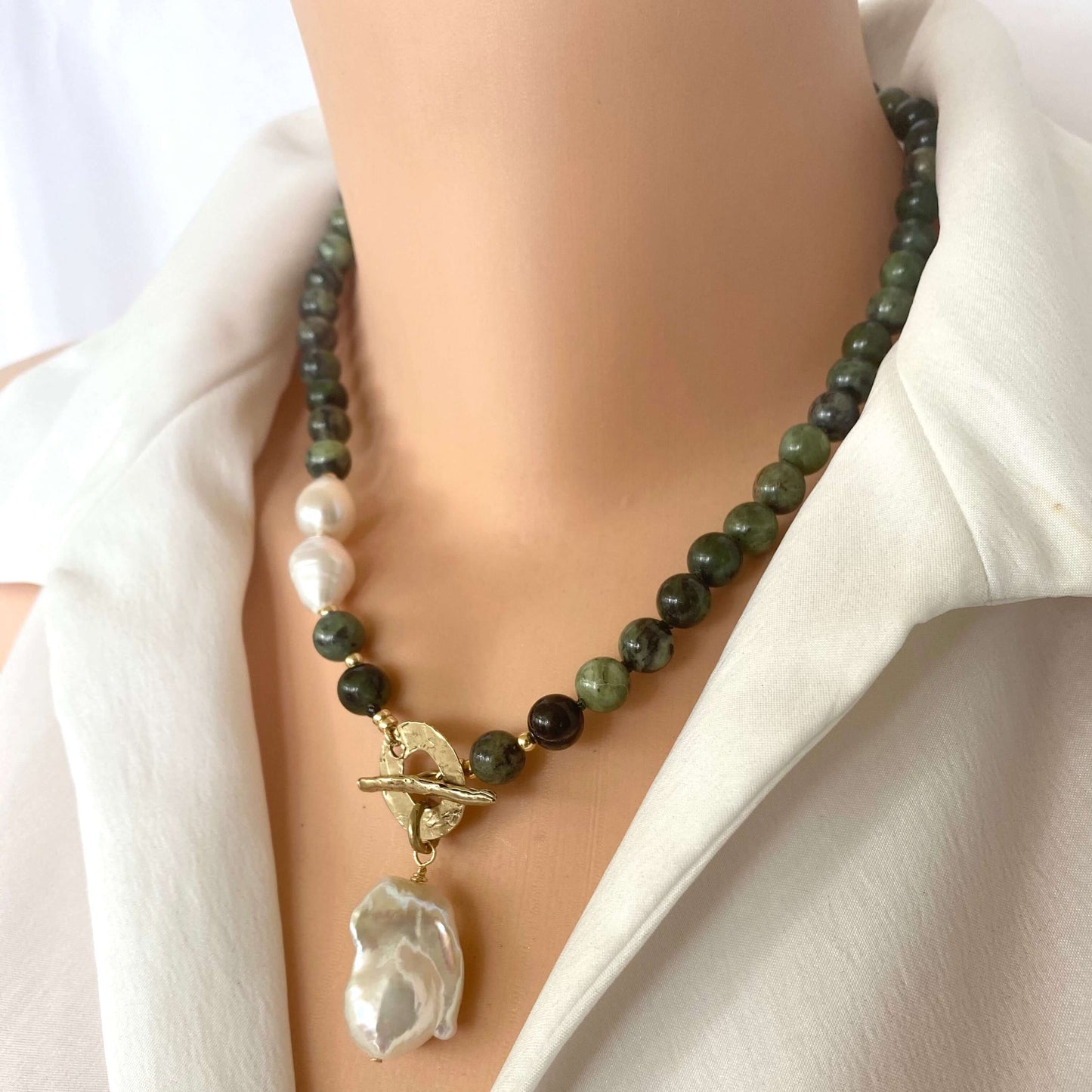 Necklace with green beads and a large white pearl pendant on a mannequin wearing a white shirt.