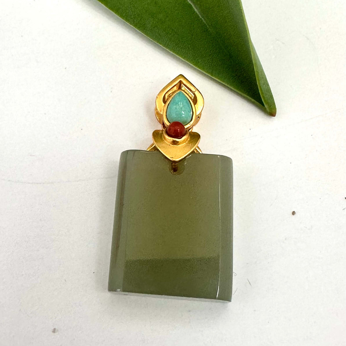 Hotan jade pendant with turquoise and red agate in gold vermeil on a plain background.
