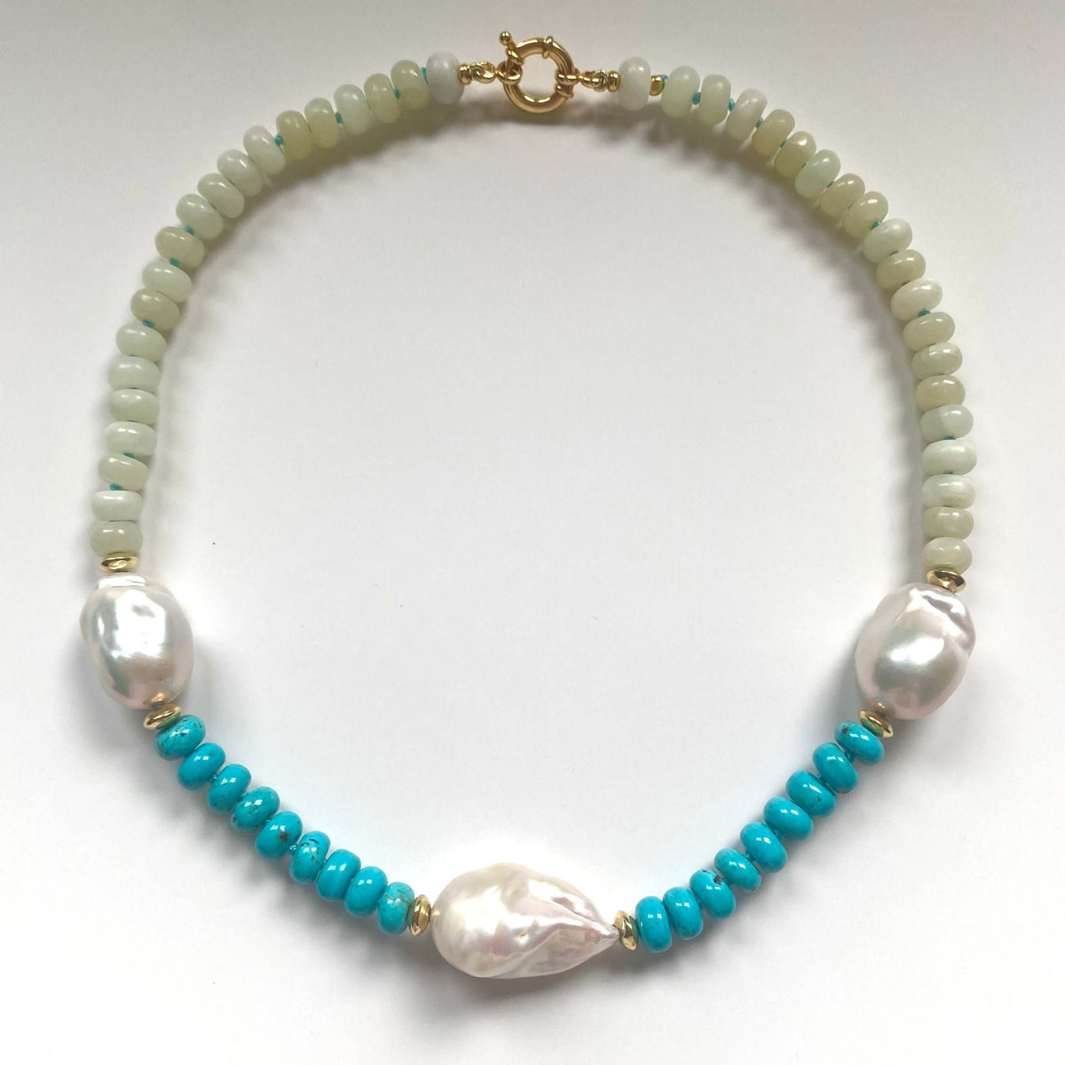 A beaded necklace featuring light green beads, white baroque pearls, and bright turquoise blue beads separated by small gold spacer beads, displayed on a clean white background.