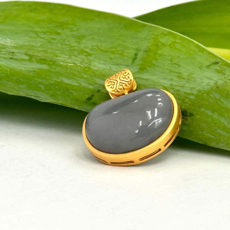 Hotan jade charm pendant in gold bezel resting on a green leaf, featuring a smooth nephrite jade teardrop.