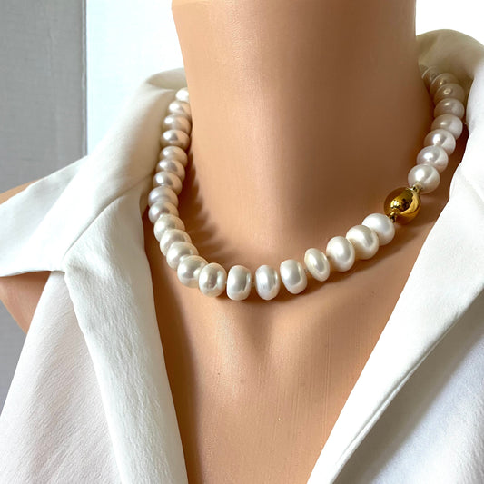 A close-up of a pearl necklace with a single gold bead accent, displayed on a mannequin torso wearing a white blouse.