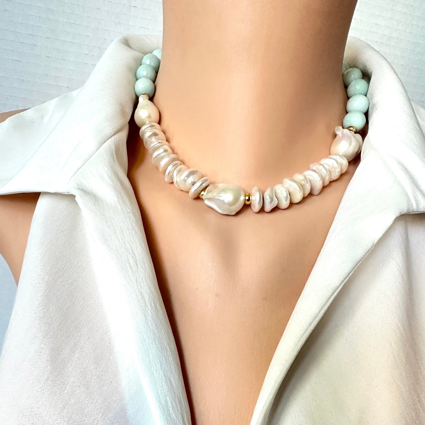 A close-up of a model wearing a double-strand statement necklace. The necklace features a strand of irregular, baroque-style cream pearls and a second strand of smooth, pale mint green beads, separated by small gold spacer rings.
