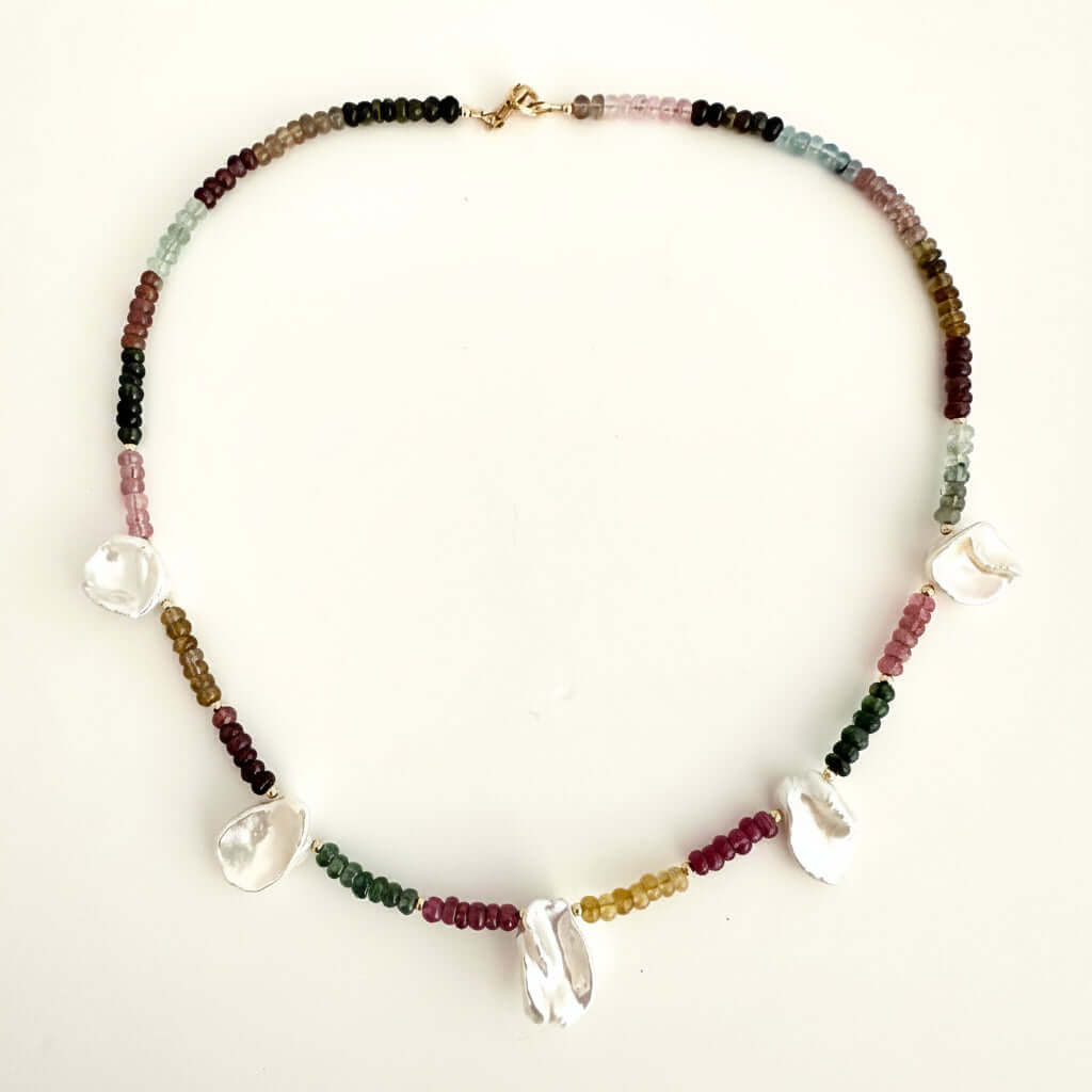 A beaded necklace with small multicolored tourmaline beads and 5 white pearl charms, displayed on a plain off-white background.