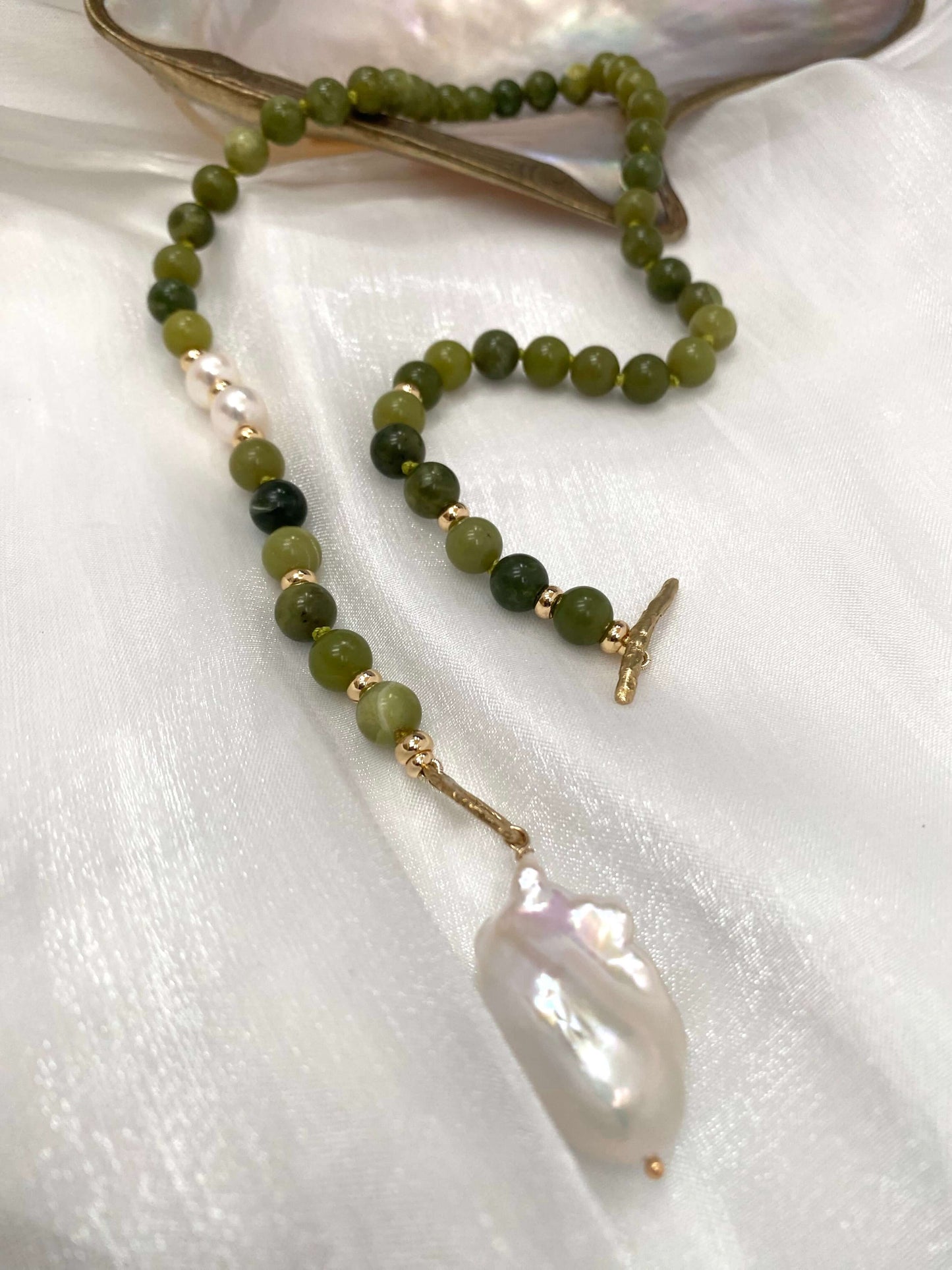 Necklace with green beads and a large white pearl on a white fabric background