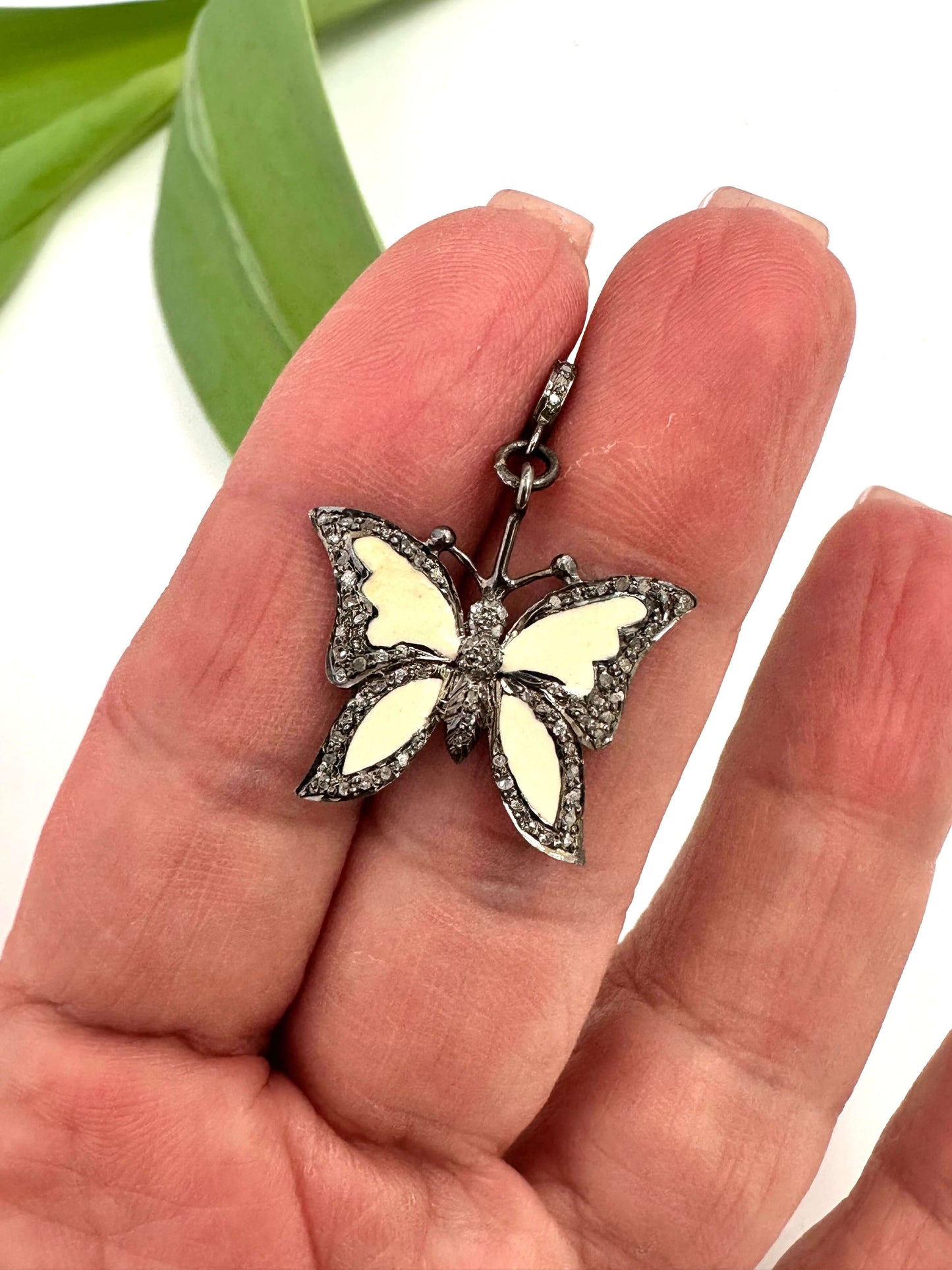 Enamel butterfly pendant with diamond pavé in sterling silver held in hand, showcasing soft off-white enamel wings and sparkling details.
