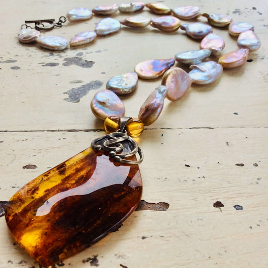 Keshi pearl necklace with amber pendant displayed on white wooden table, close-up view.