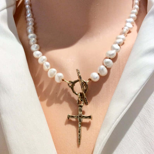 Pearl necklace with a gold cross pendant worn by a person in a white outfit.