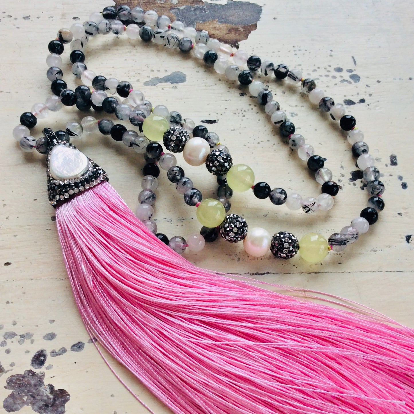 Rutilated quartz necklace with long pink silk tassel pendant photographed in sunlight.