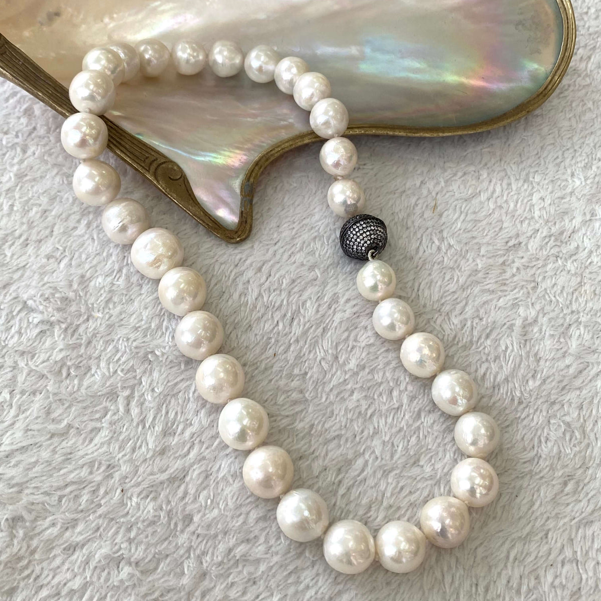 White Edison pearl necklace with gunmetal pavé magnetic clasp displayed on an iridescent shell.