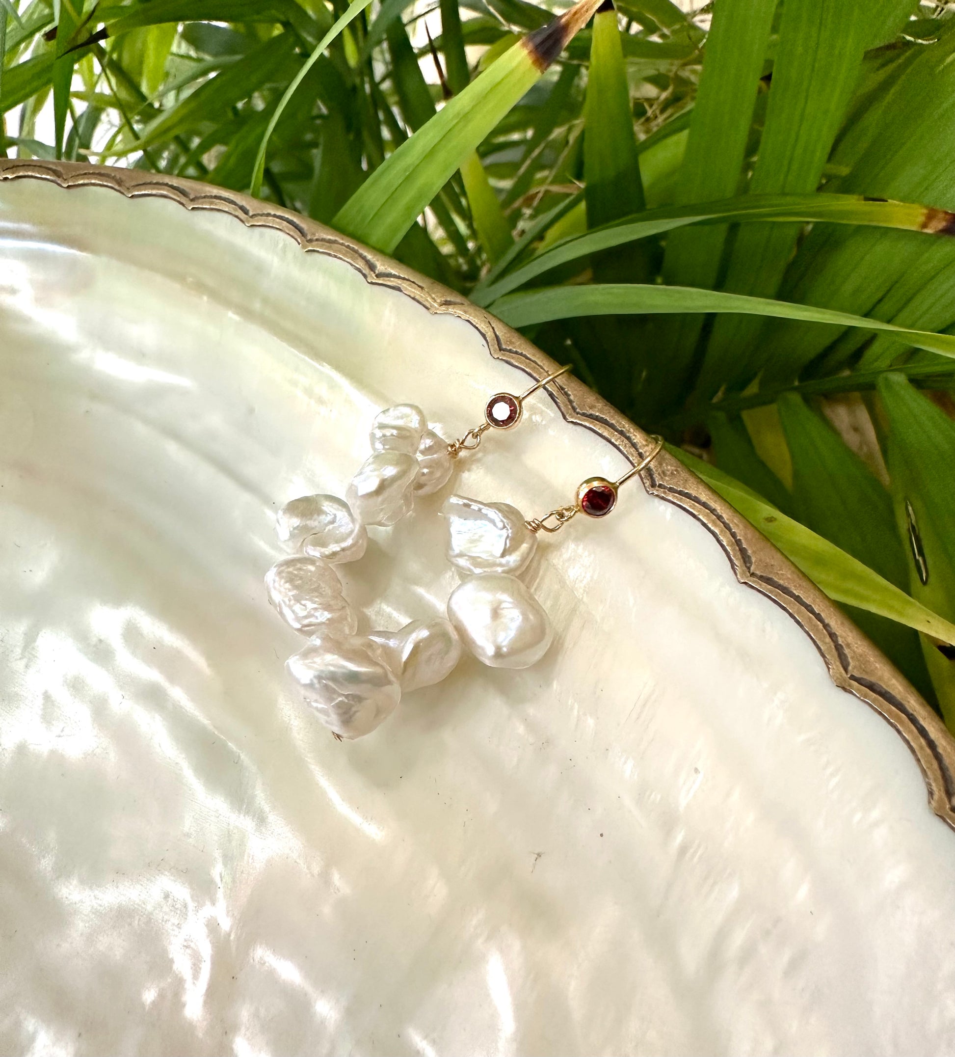 Pearl drop earrings featuring keshi pearls and red CZ, displayed on a decorative plate with greenery.