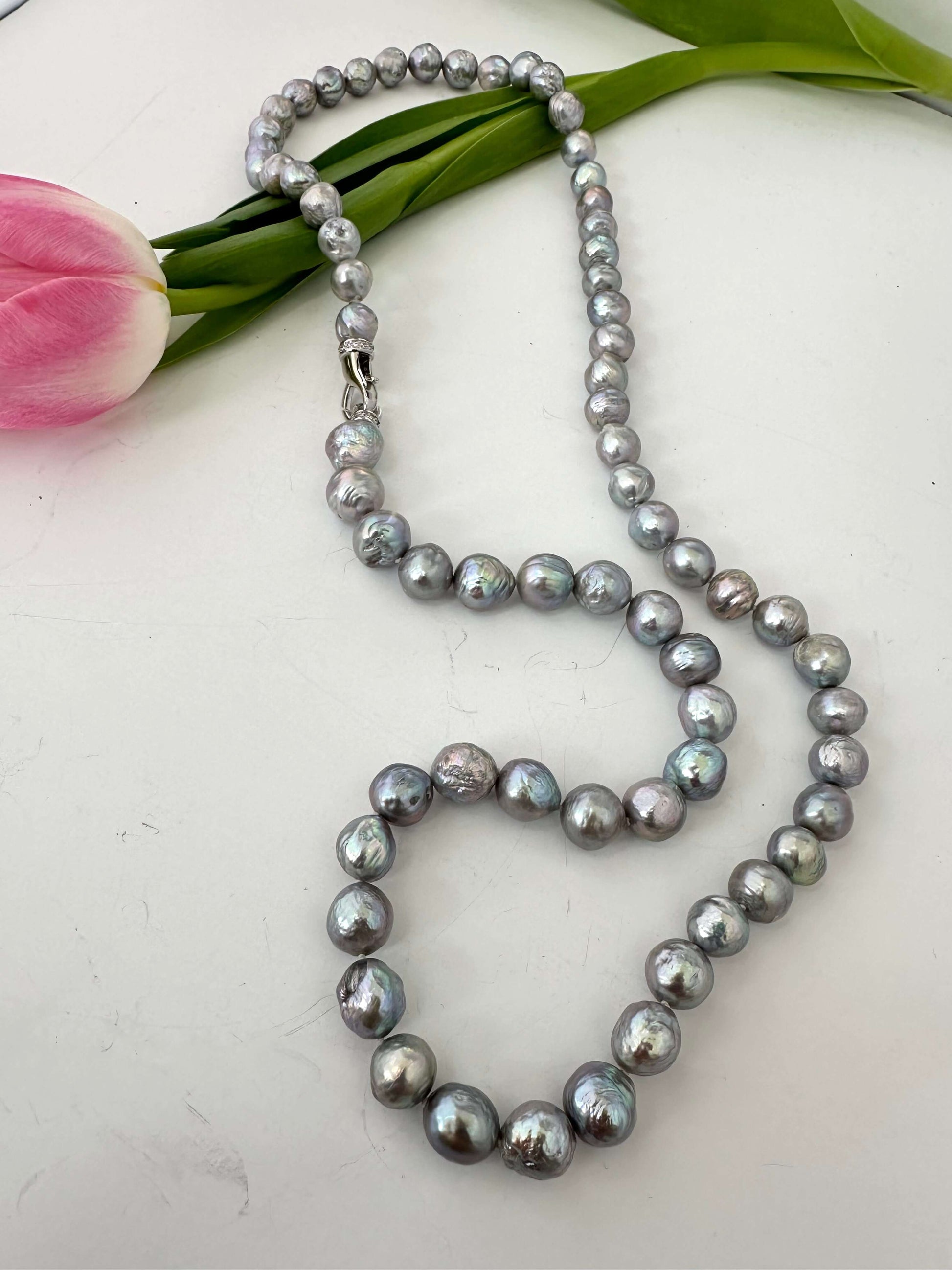 Pearl necklace on a white surface with a pink tulip