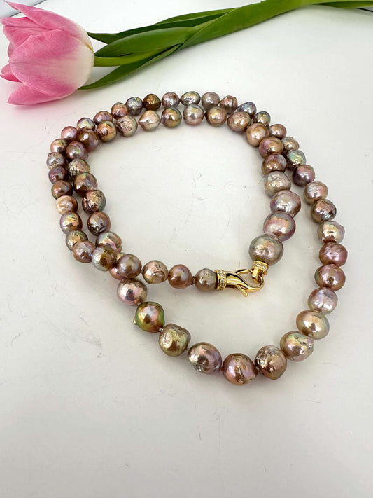 Pearl necklace with a gold clasp on a white surface with a pink tulip.