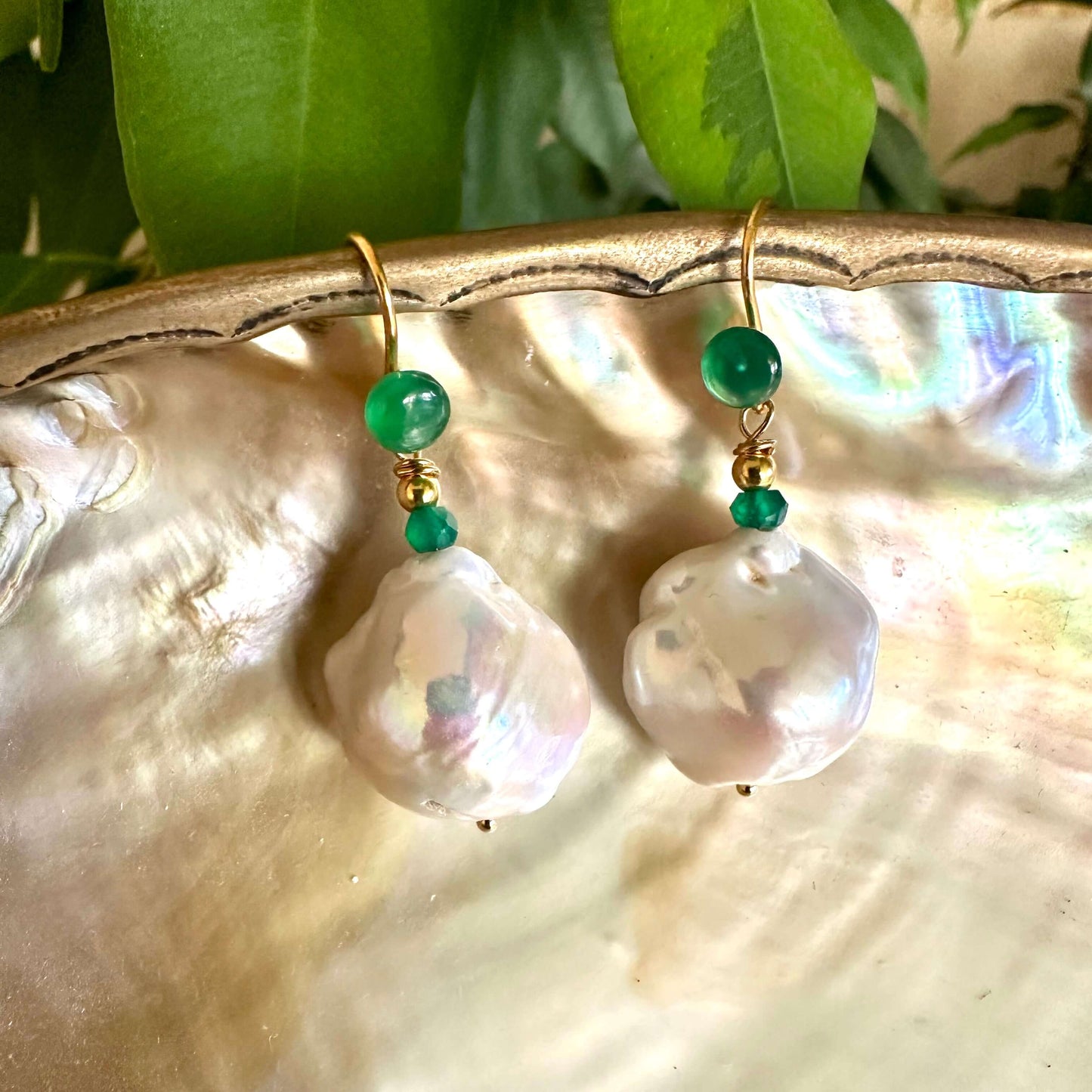 White baroque pearl drop earrings with green agate on a decorative background.