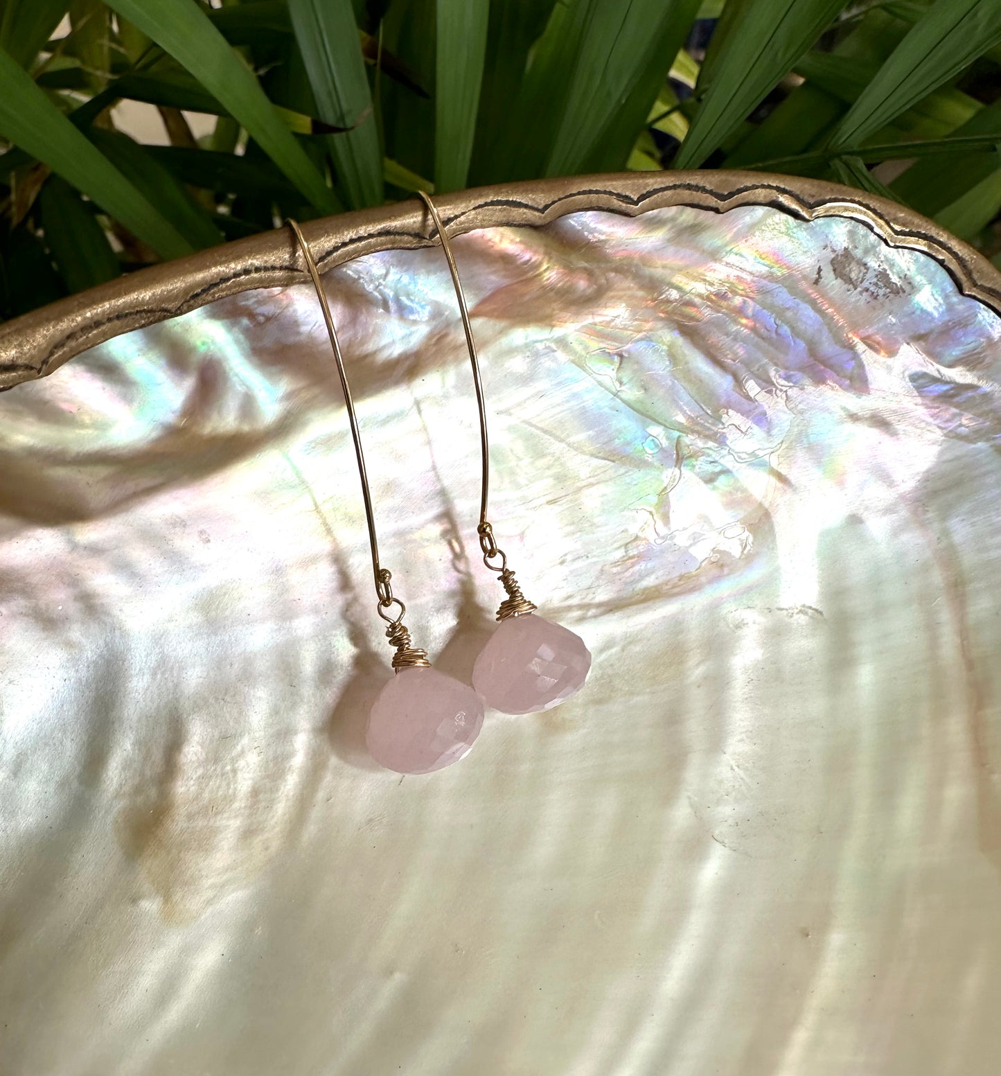 Rose quartz threader earrings with briolettes on a decorative shell background.