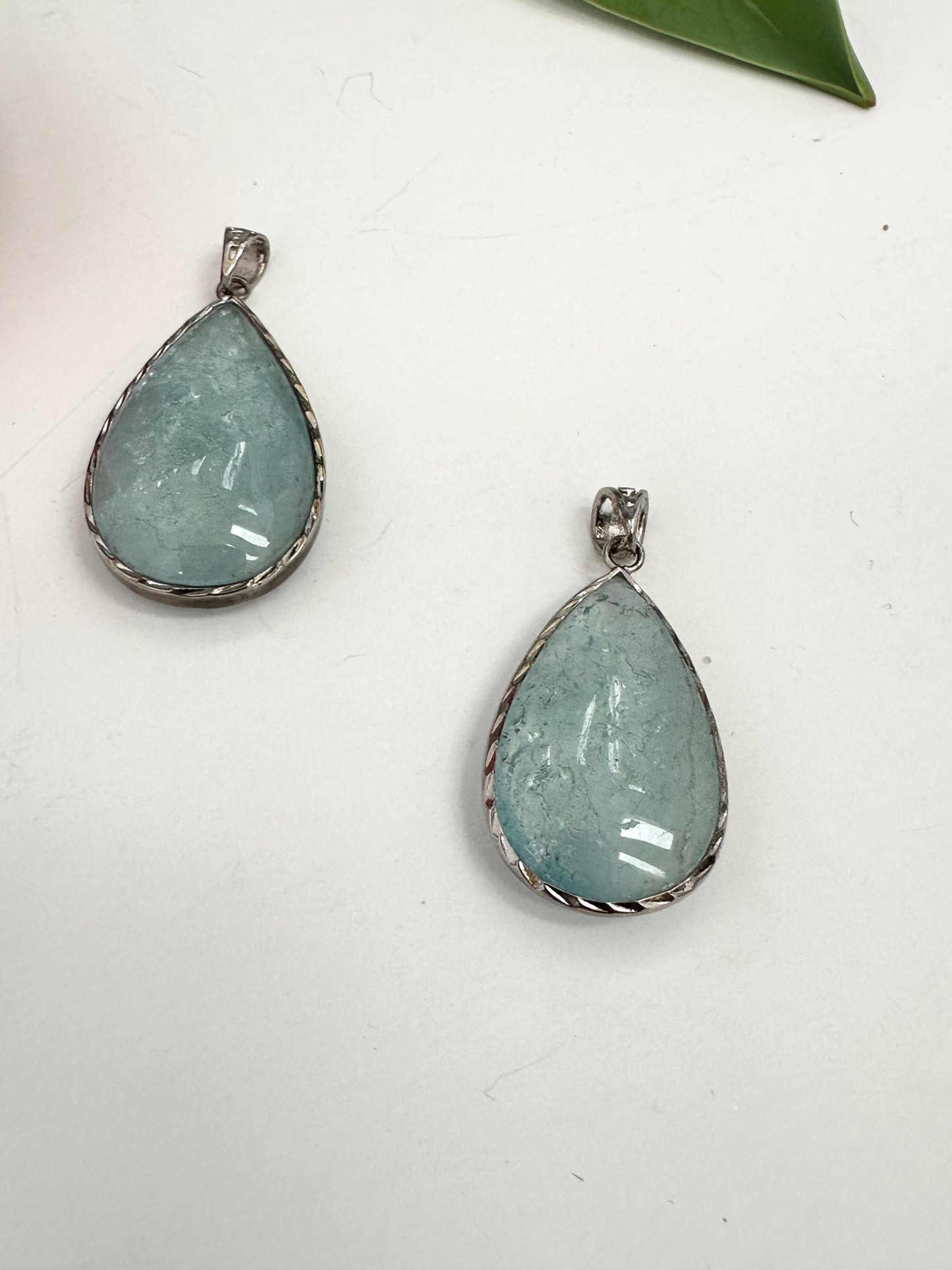 Two teardrop-shaped pendants with a light blue gemstone on a white background.
