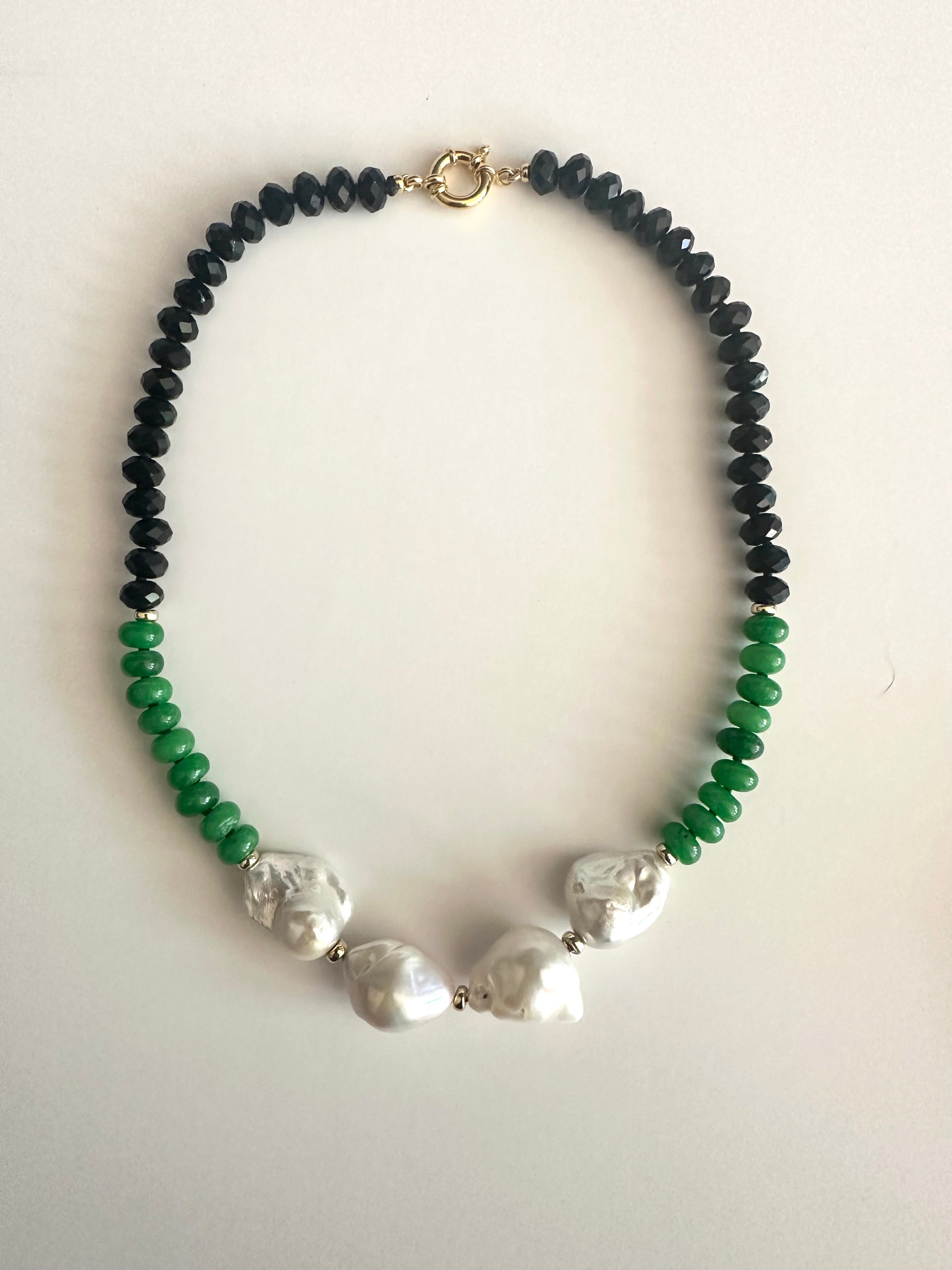 A beaded necklace with black faceted beads on the top half, green faceted beads on the bottom half, and 4 large white baroque pearls in the center, finished with a SILVER clasp, shown on a light beige background.