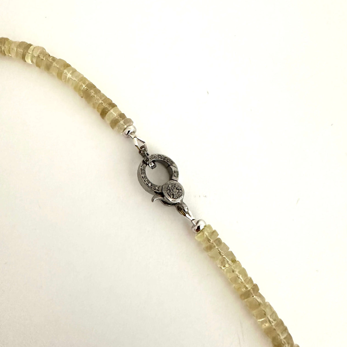 A close-up of a beaded necklace with faceted pale yellow-green beads and a silver-toned circular clasp on a plain white background.