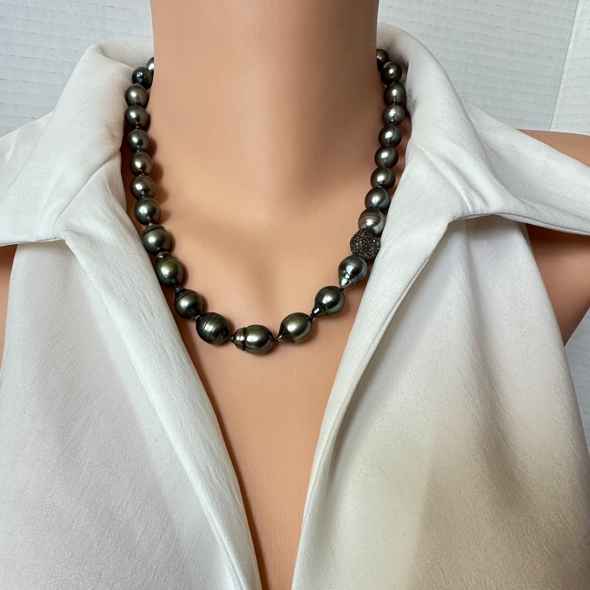 A dark gray baroque pearl necklace displayed on a mannequin torso wearing a white satin blouse.