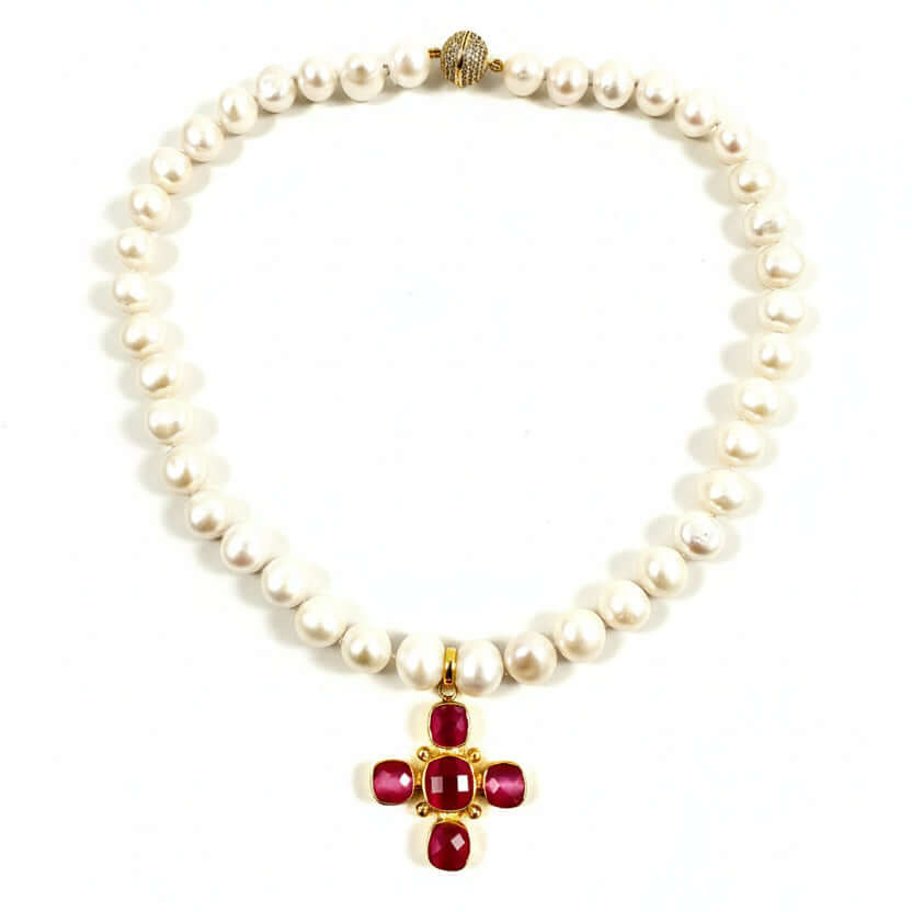 A pearl necklace with a gold cross pendant featuring red gemstone accents, displayed on a clean off-white background.