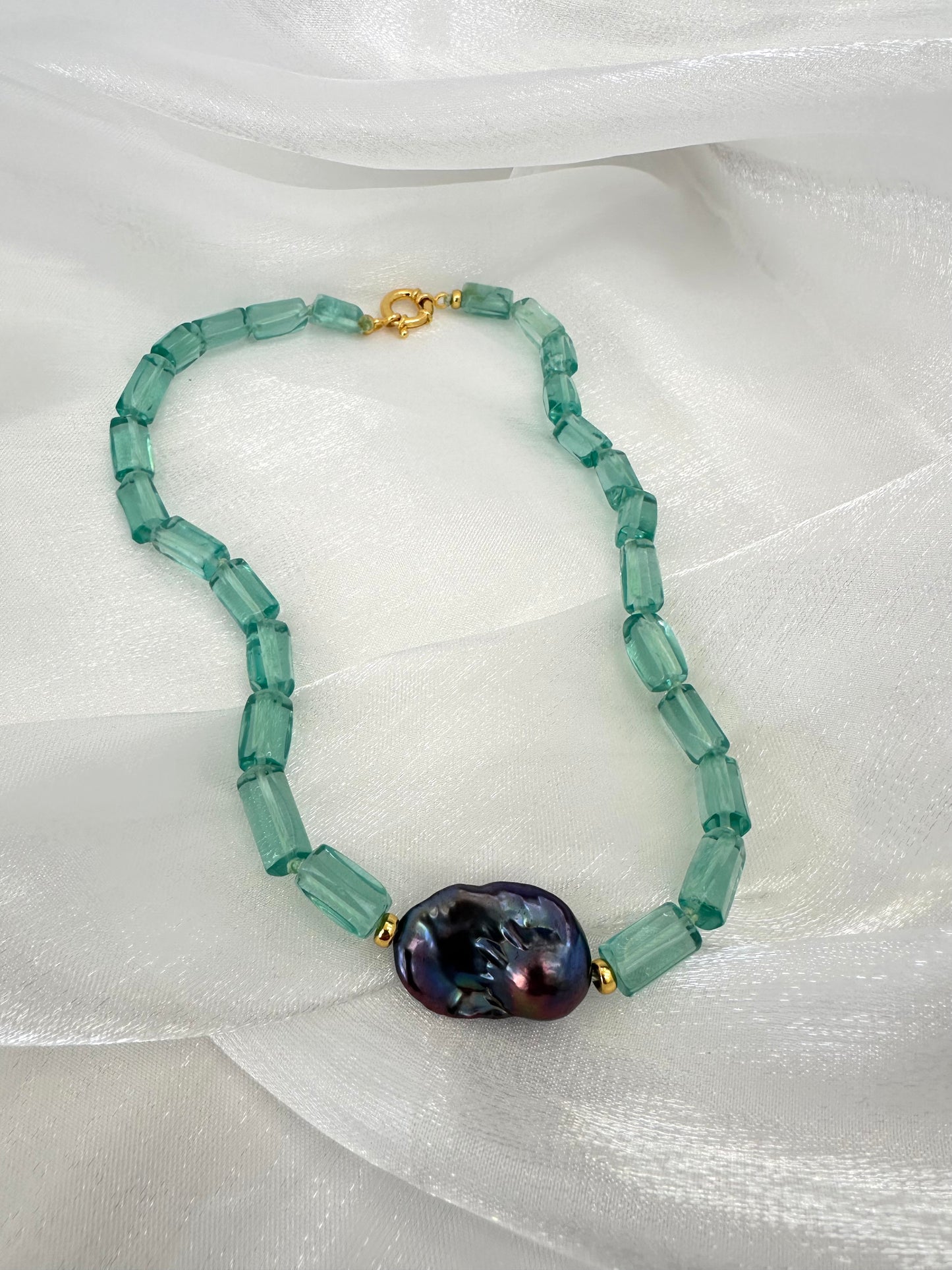 Necklace with green beads and a large purple bead on a white fabric background