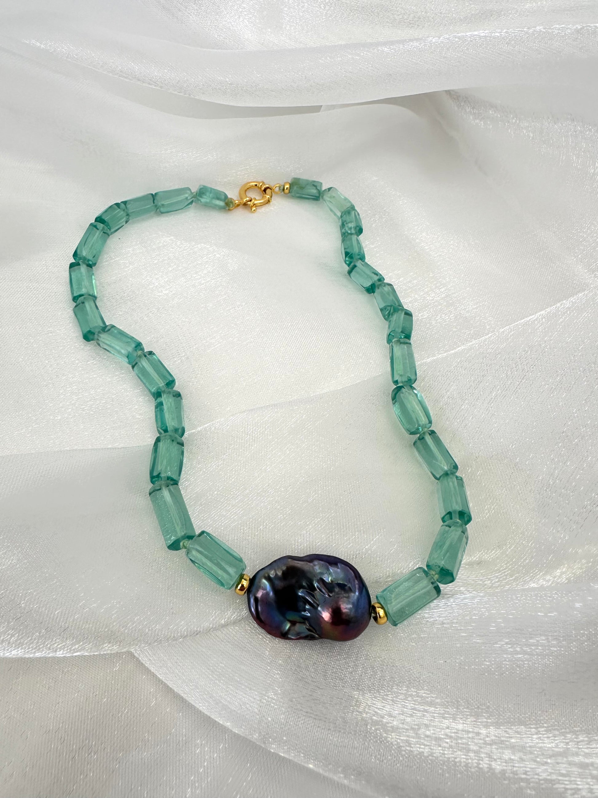 Necklace with green beads and a large purple bead on a white fabric background