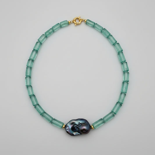 Necklace with green beads and a large purple bead on a white fabric background