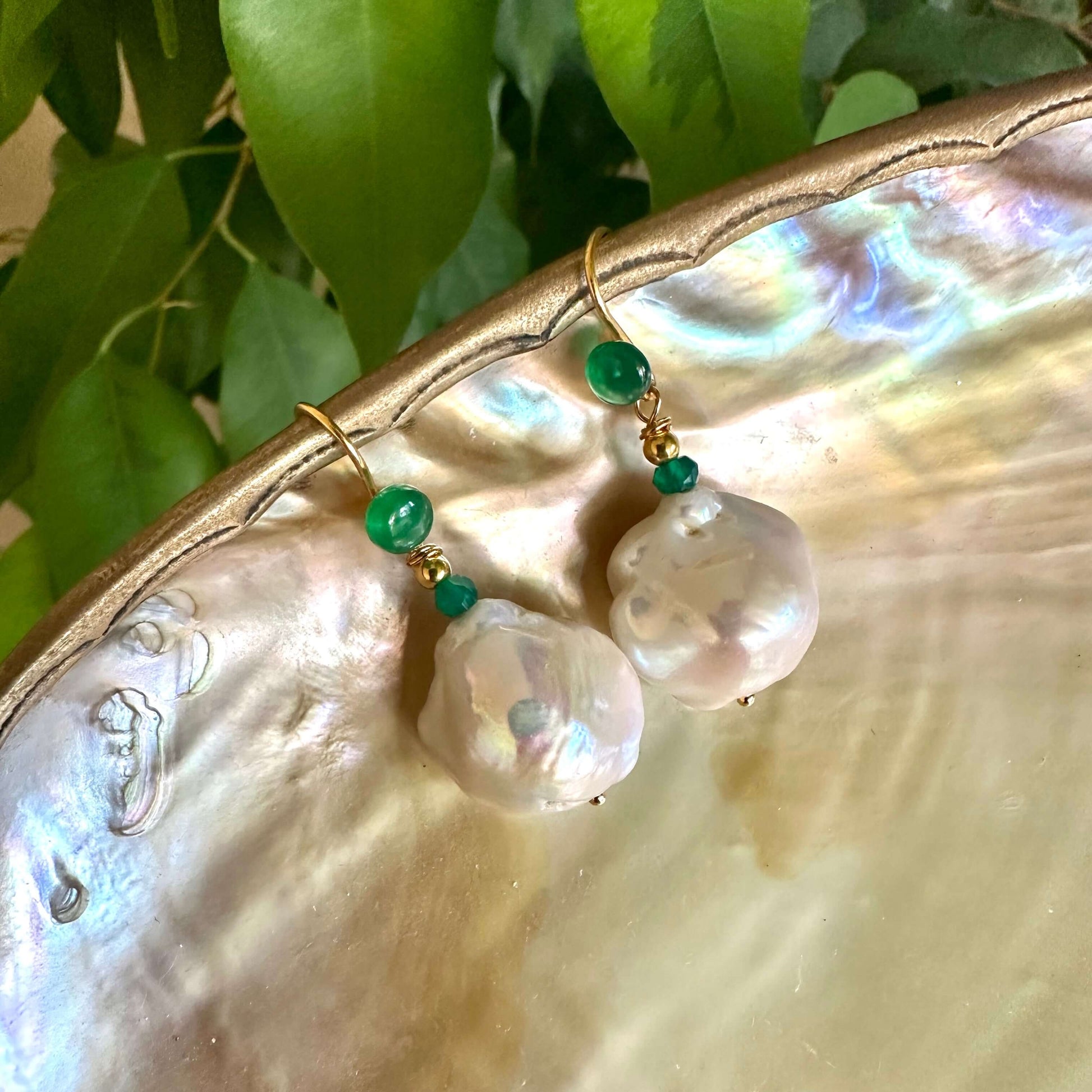 White baroque pearl drop earrings with green agate on a shell background, showcasing elegant and unique design.