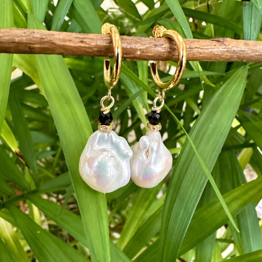 Close-up of white baroque pearl hoop earrings dangling from branch with green foliage background
