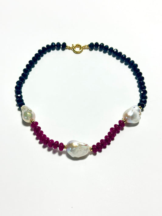 A beaded necklace featuring BLACK  faceted beads, deep magenta red beads, and three large white baroque pearls, finished with a gold clasp, shown on a plain white background.