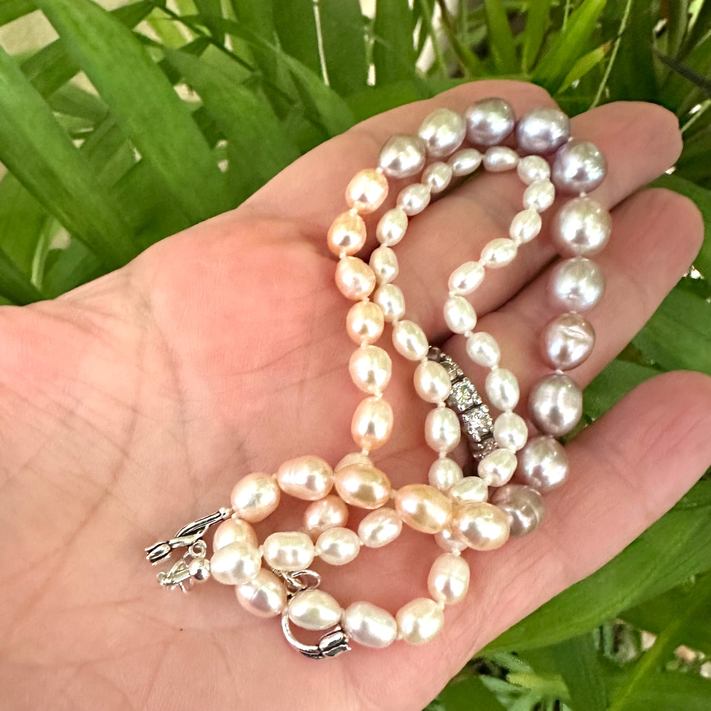 Pastel Rice Pearl Necklace displayed in hand with natural green leaf backdrop for detail.