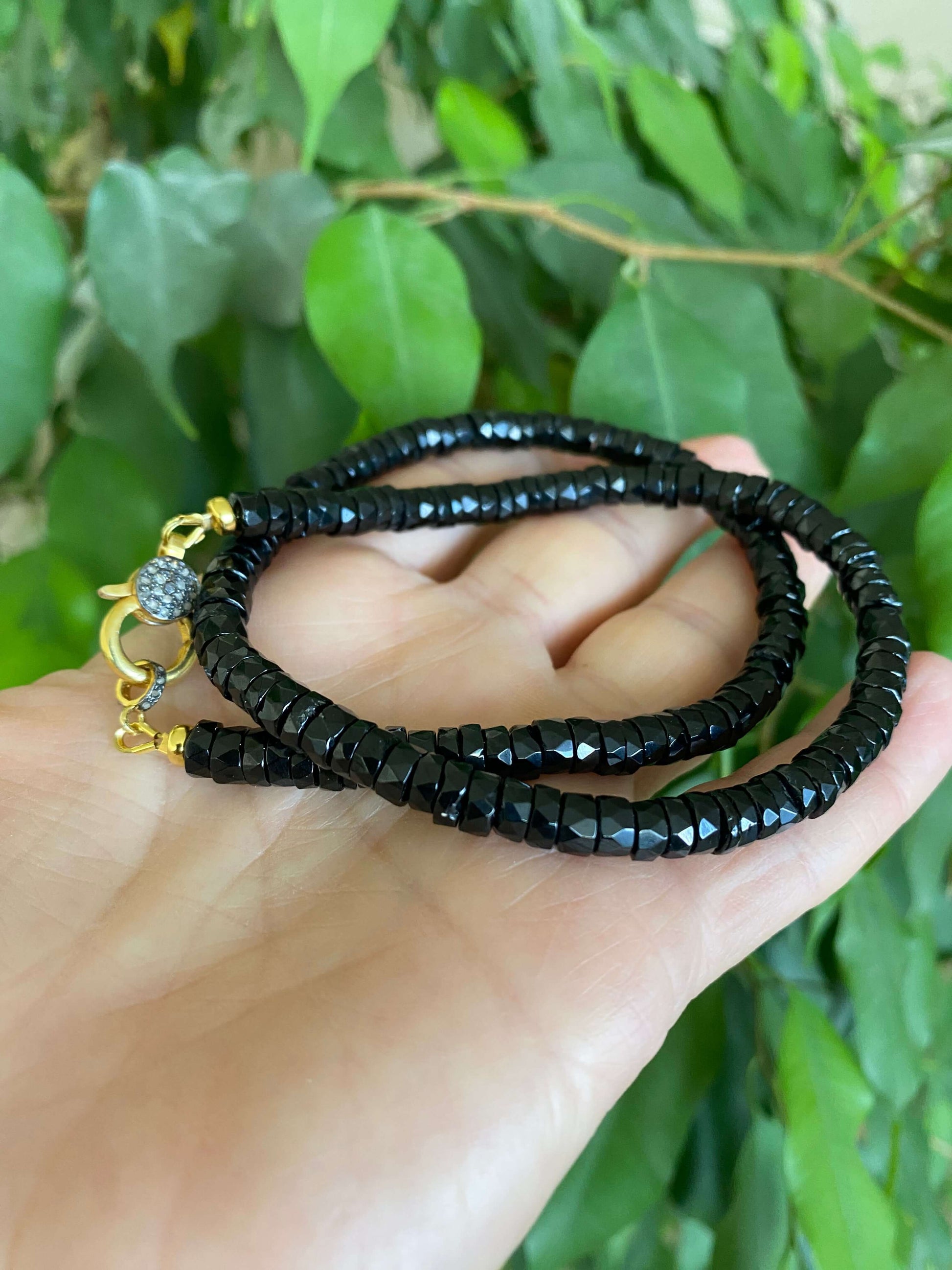 Black spinel beaded necklace showcasing black spinel heishi beads and gold vermeil pavé clasp against green background.