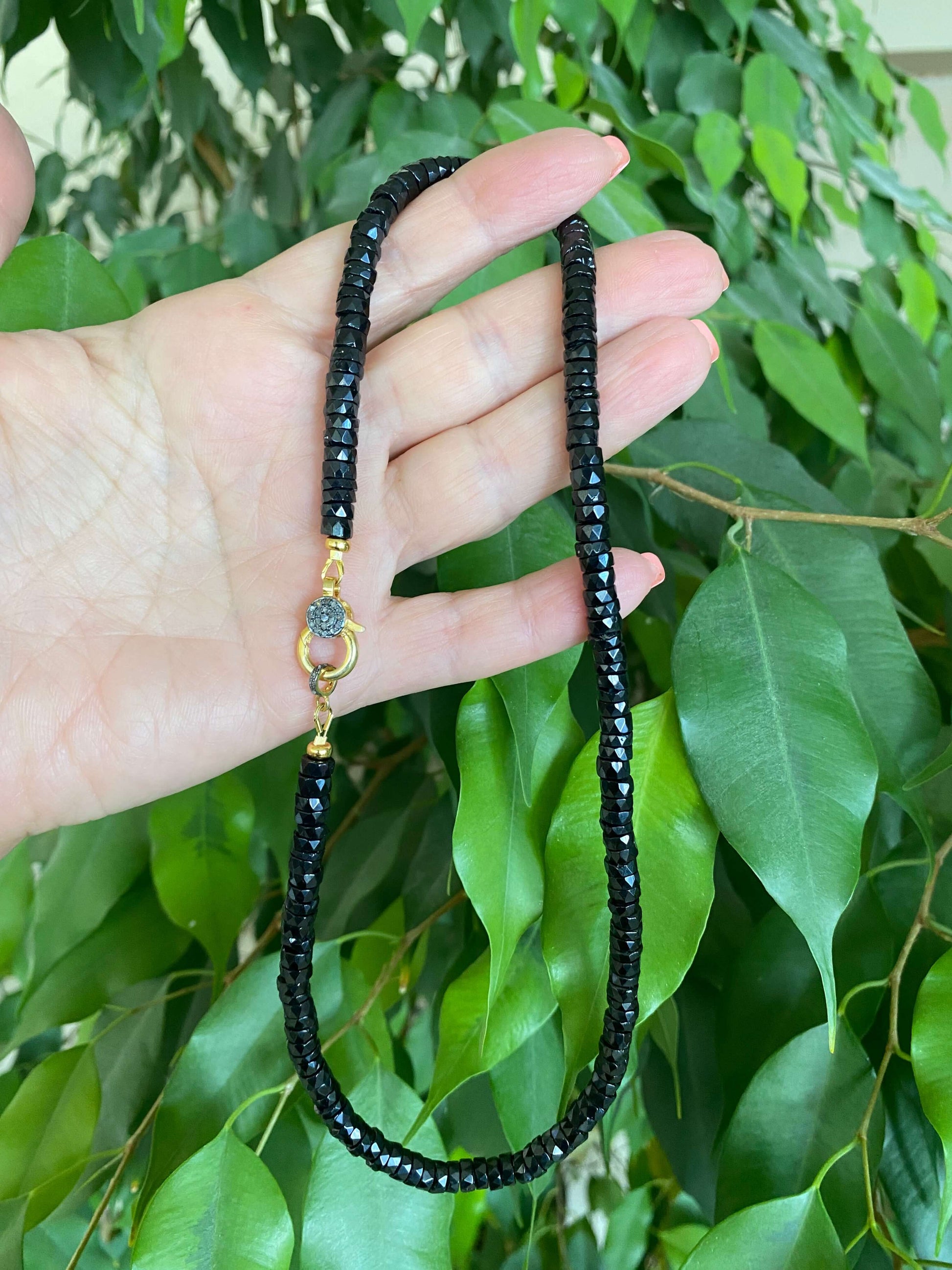 Black spinel beaded necklace with gold vermeil pavé clasp showcased against green leaves.