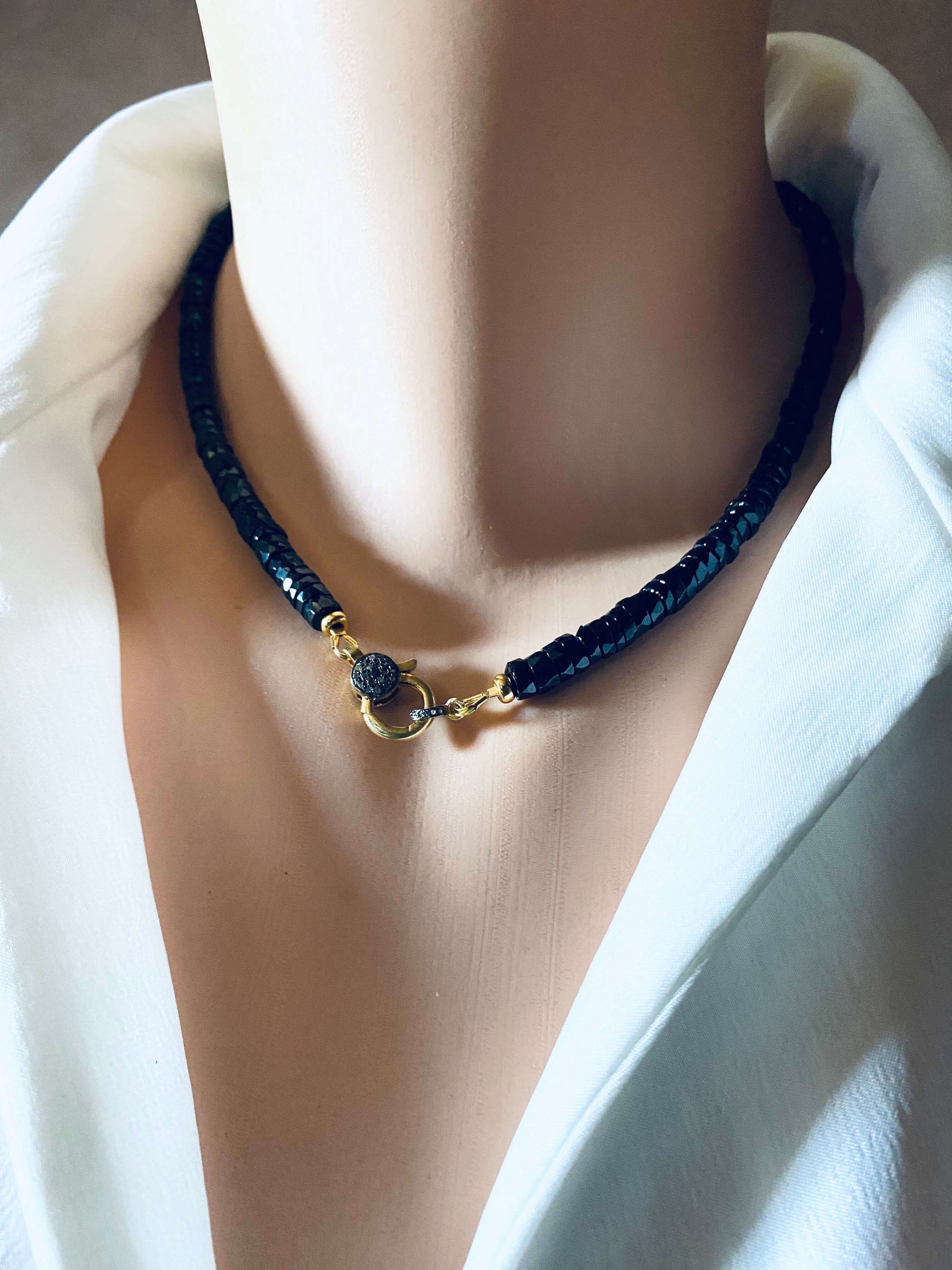 Black spinel beaded necklace with gold vermeil pavé clasp worn on a mannequin's neck, showcasing modern luxury.