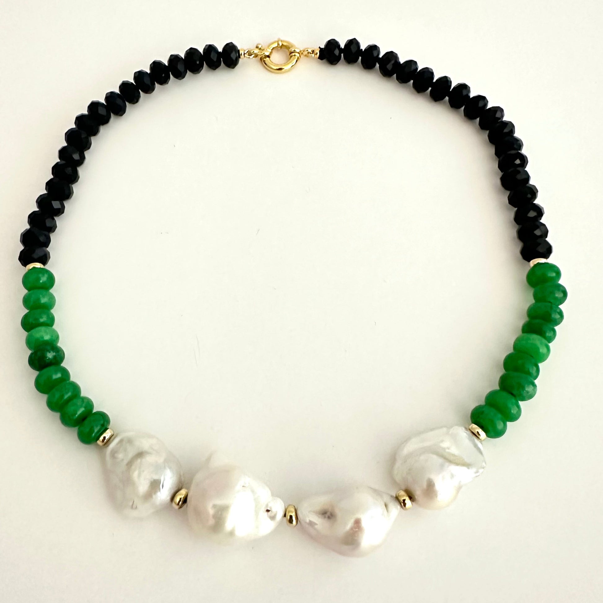 A beaded necklace featuring black faceted beads on one side, vibrant green beads on the other, and 4 large white baroque pearls in the center, separated by small gold spacers and connected by gold chain links.