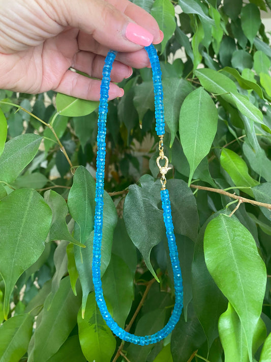 Blue topaz beaded necklace with gold vermeil pavé clasp held against lush green leaves.