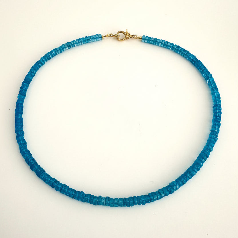 A beaded necklace made of small, faceted blue glass beads with a gold clasp, displayed on a plain white background.