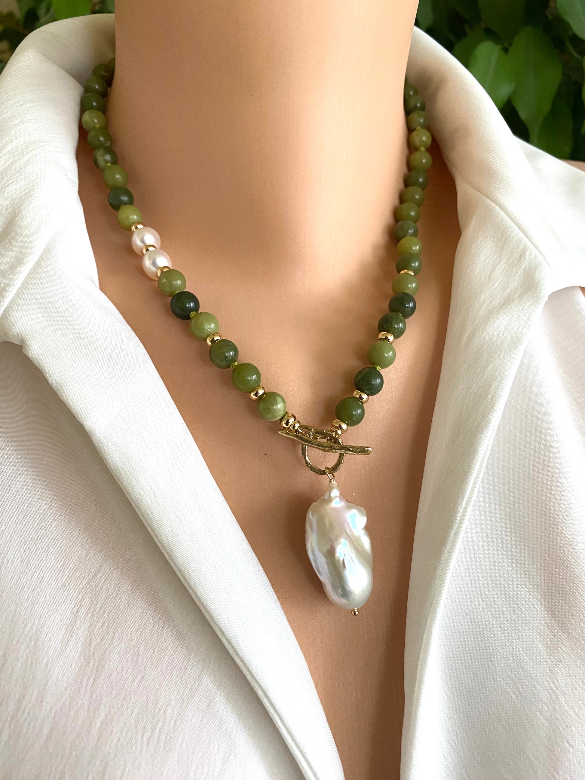 Necklace with green beads and a large white pearl on a mannequin wearing a white shirt.