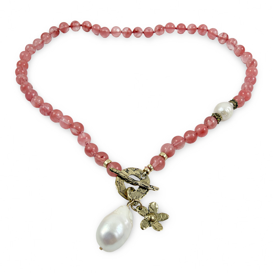A beaded necklace made of round dusty pink beads, featuring a toggle clasp with a small bird and floral charm, and a large white baroque pearl drop pendant, shown on a plain white background.