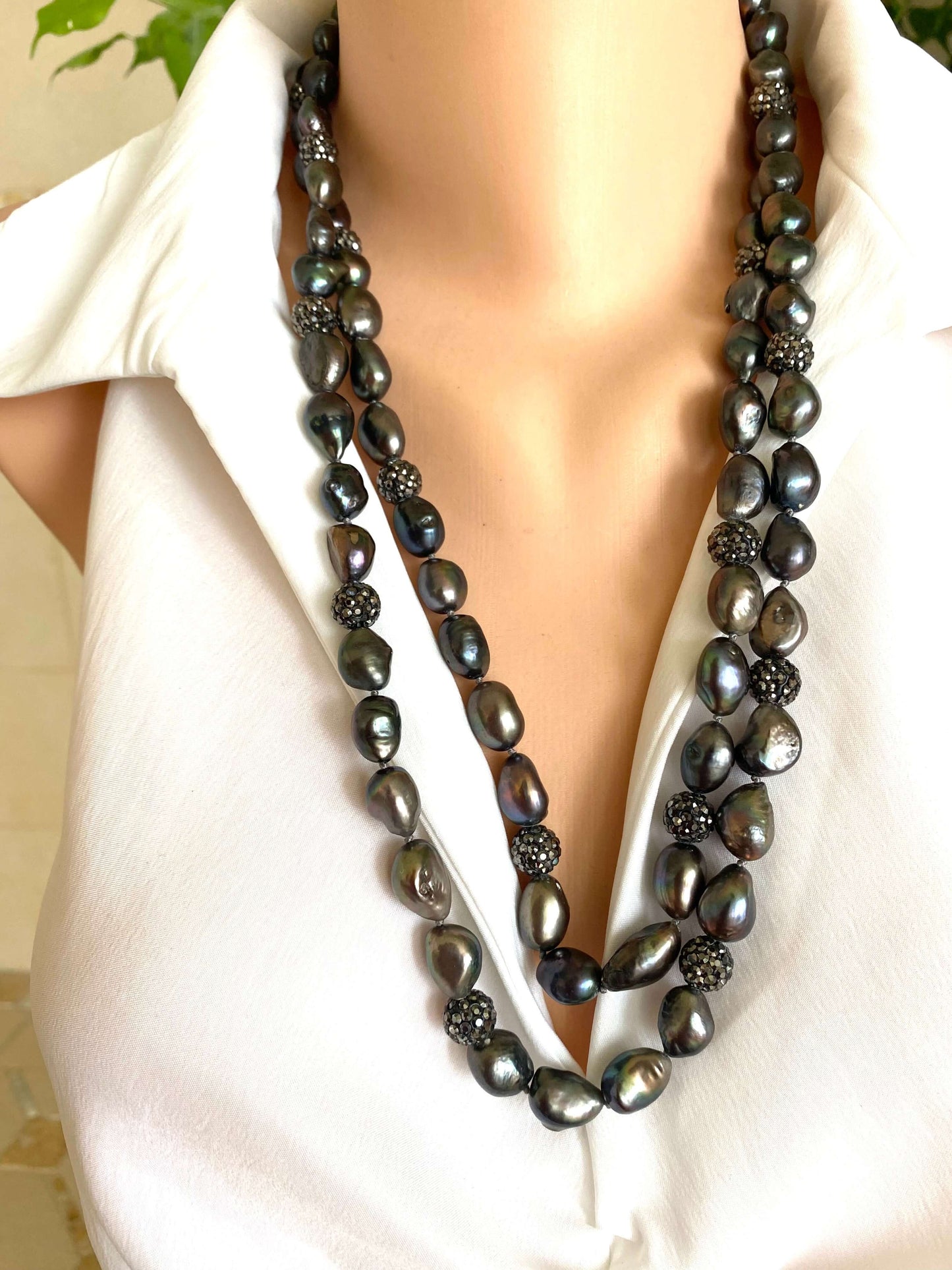 Long black pearl necklace worn by a person in a white outfit.