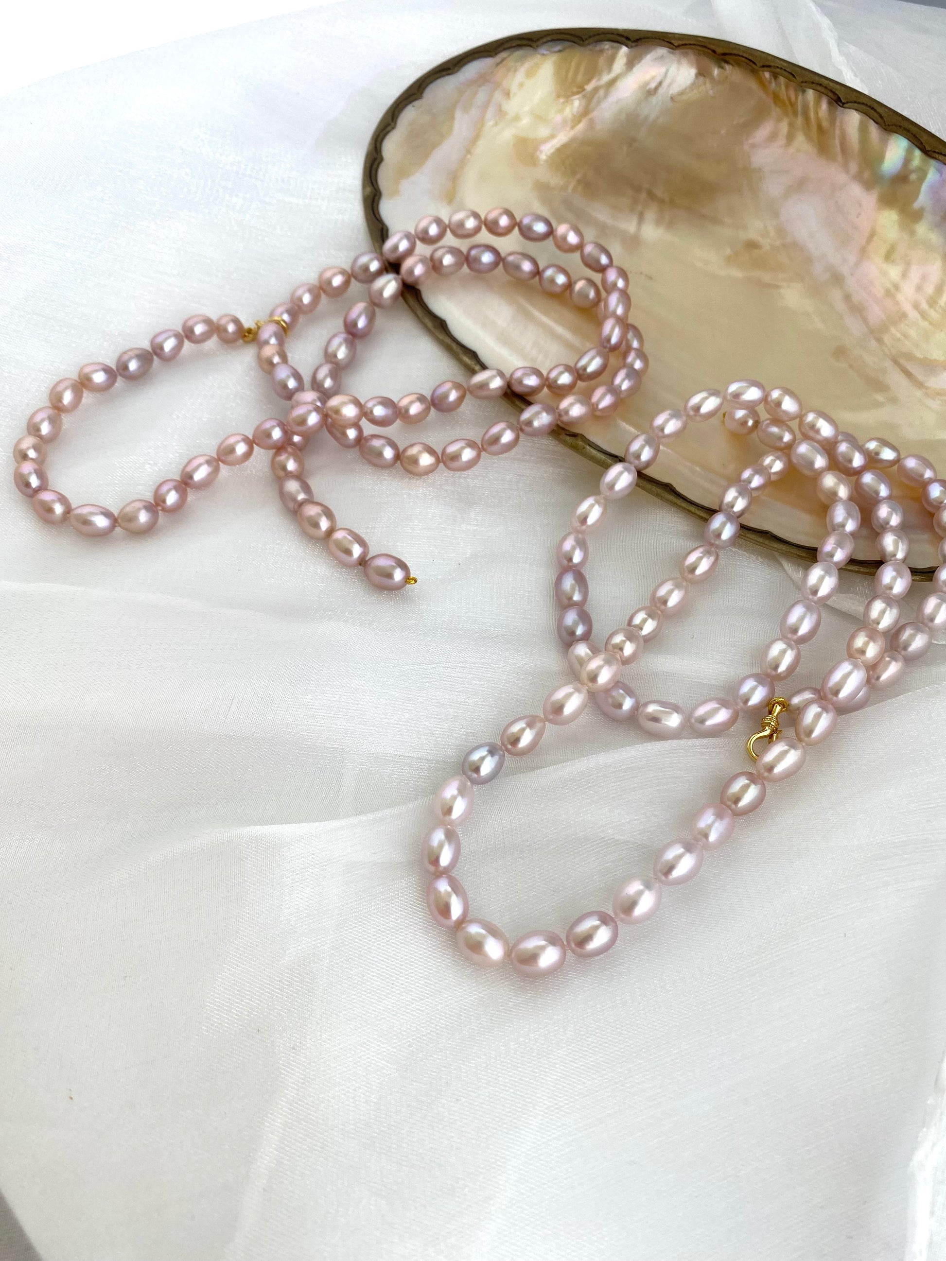 Pearl necklace draped over a shell on a white surface