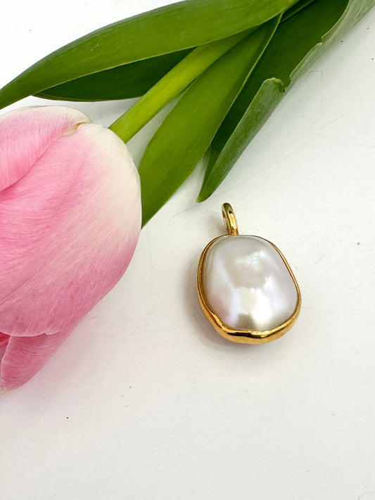 Gold pendant with a large pearl on a white surface with pink tulip and green leaves.